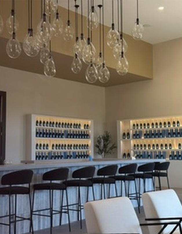 Bar stools lined along Petit Domaine’s champagne bar, with backlit shelves of sparkling wine behind