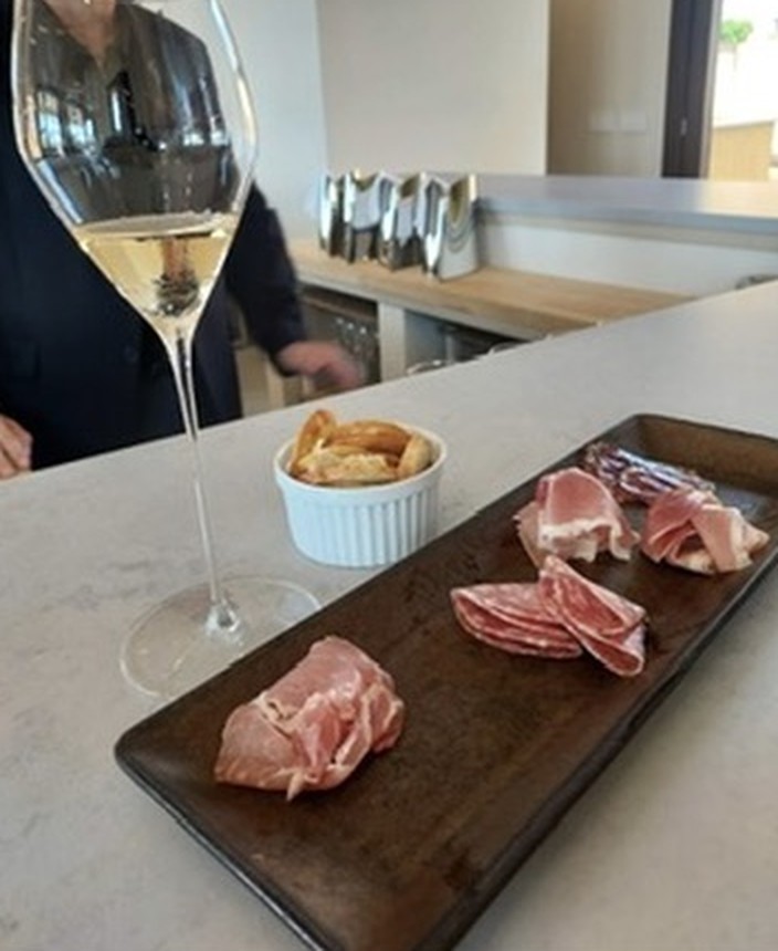 A glass of sparkling wine beside a board of cured meats and crackers on the bar