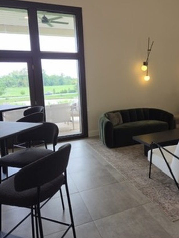 The tasting room lounge with a curved green velvet sofa, a white armchair and tall windows overlooking the estate